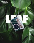 Necklace with green mini camera pendant on a leafy background, featuring the brand 'nature cosmos'.